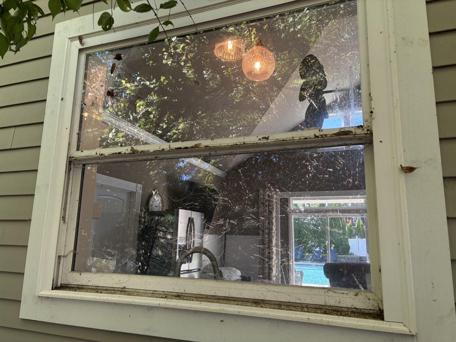 Before cleaning: Window reflecting hanging lights beside light-colored siding